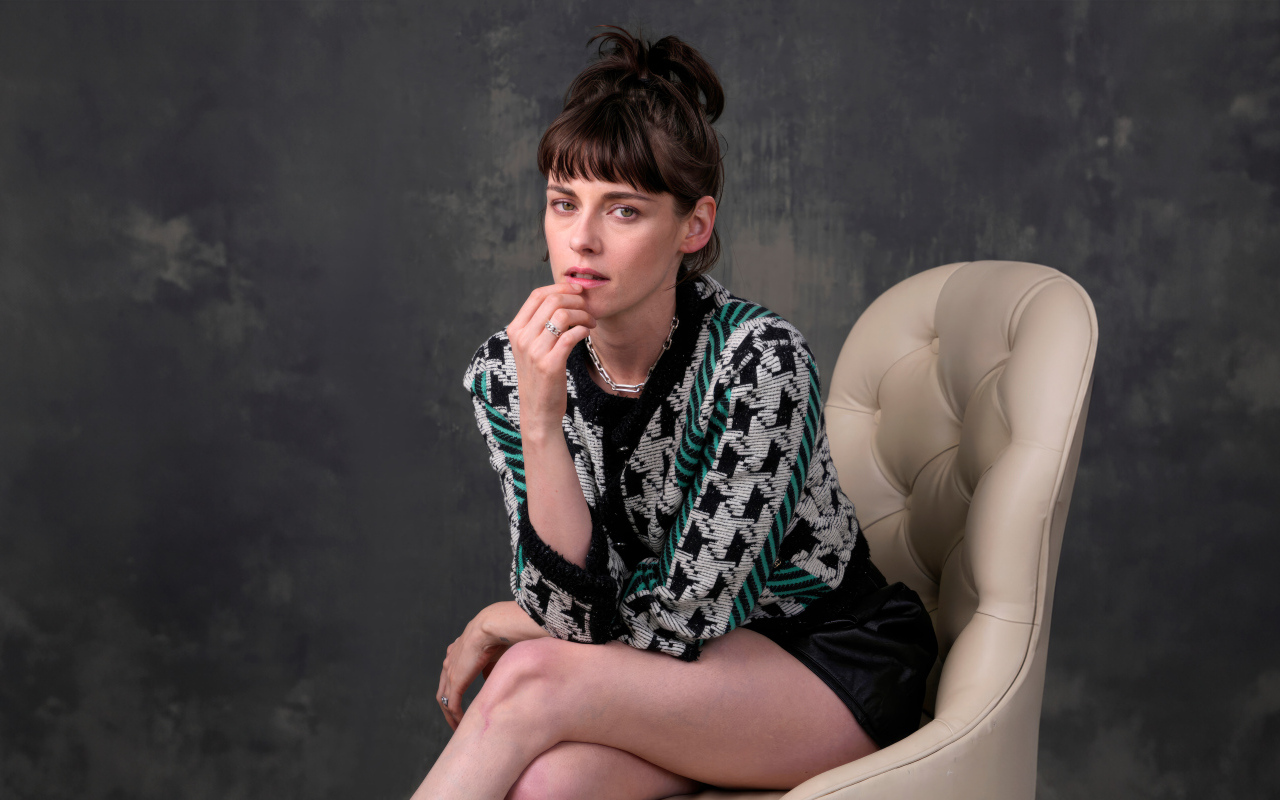 Актриса Кристен Стюарт сидит в кресле на фоне серой стены