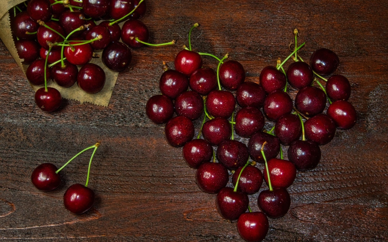 Сердце из спелых ягод черешни на деревянном столе