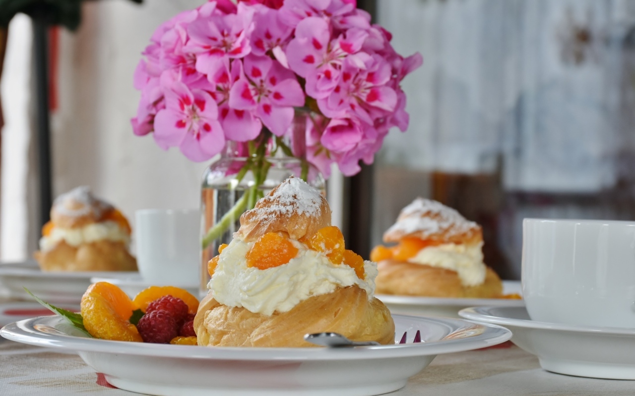 Булочки с кремом и фруктами на столе с букетом