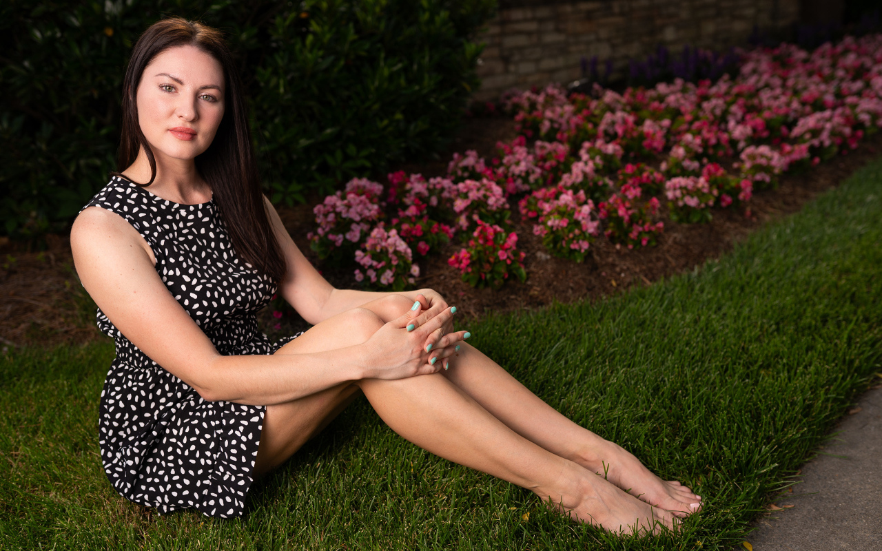 Красивая девушка в платье сидит у клумбы с цветами
