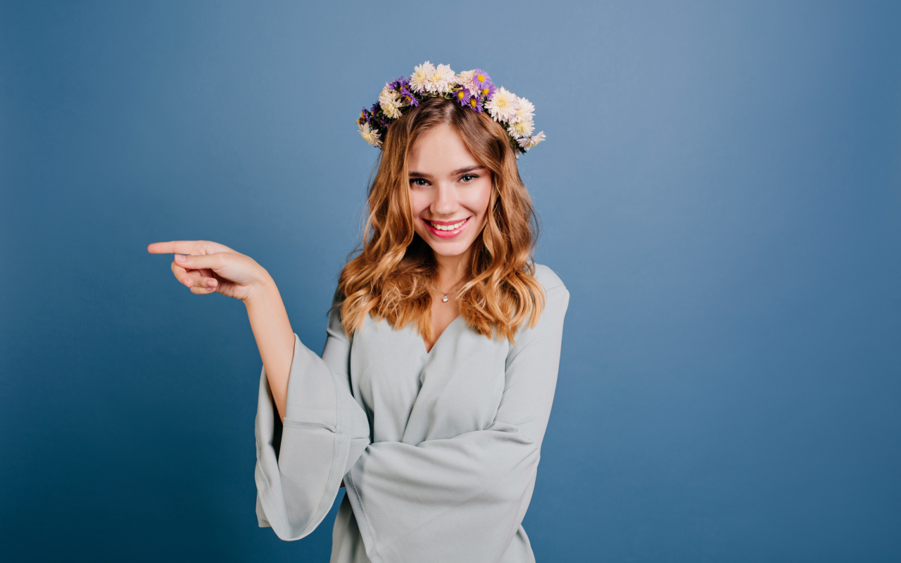 Милая улыбающаяся девушка с венком на голове на сером фоне