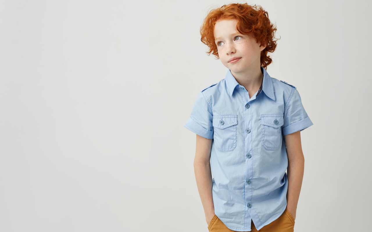 Рыжеволосый мальчик на фоне серой стены