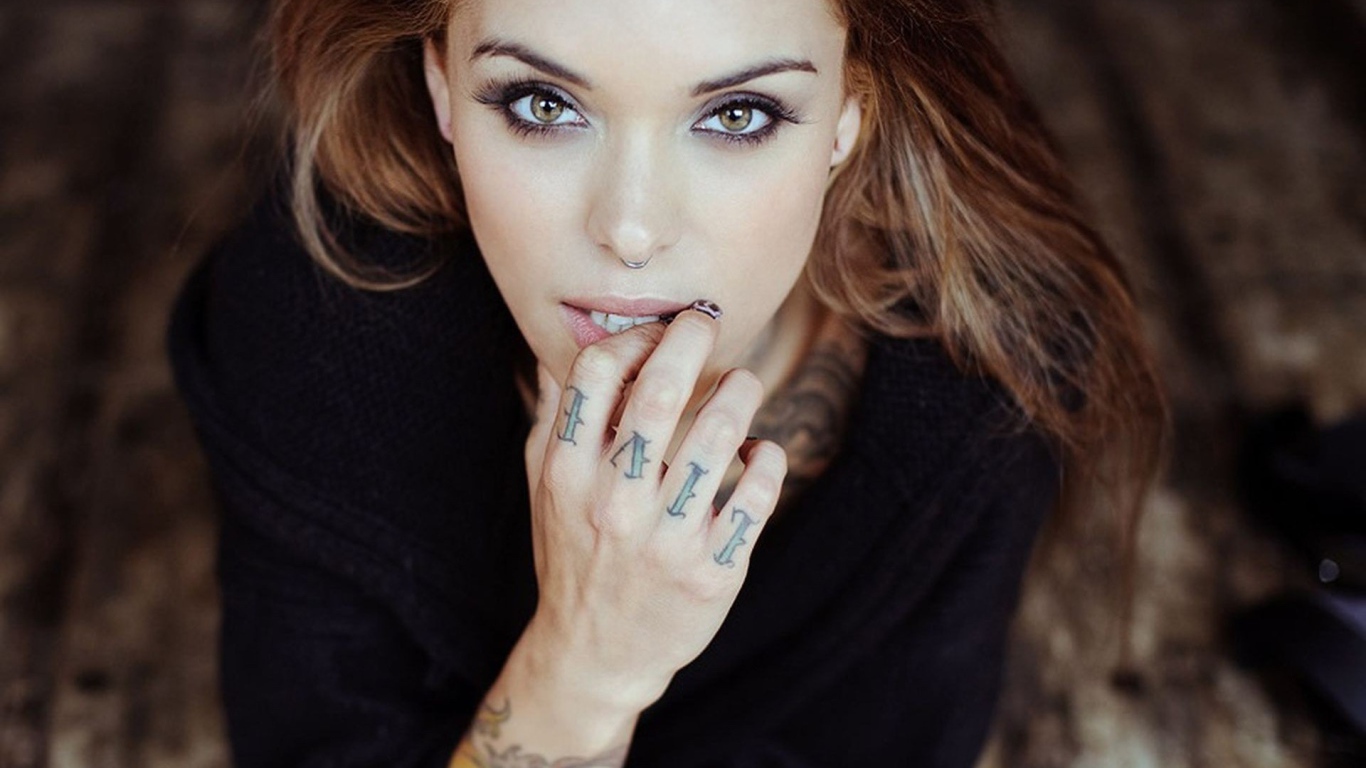Девушка шатенка с пирсингом в носу и татуировкой на руке