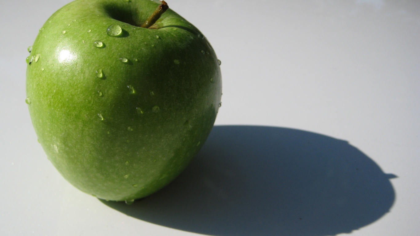 Зеленое яблоко на белой поверхности