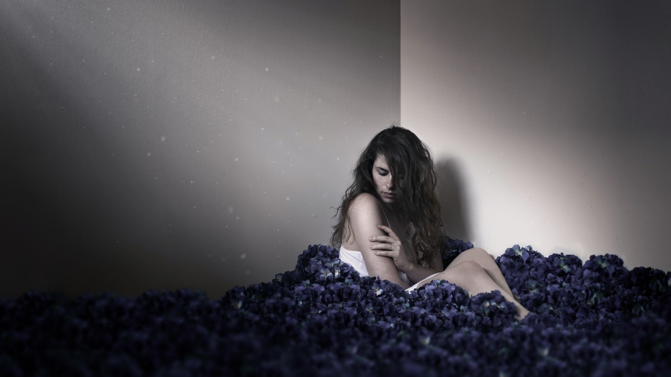 Девушка сидит в углу среди цветов