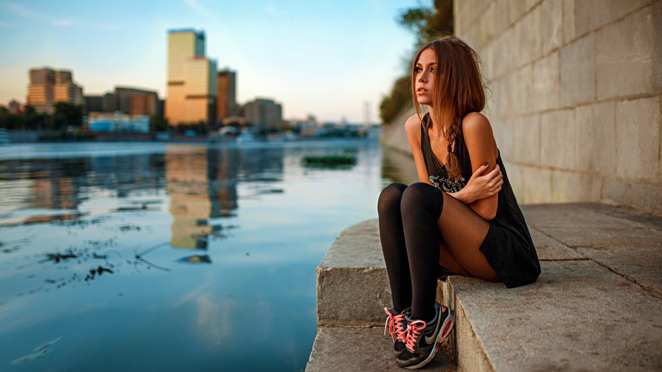 Девушка в кедах сидит на набережной