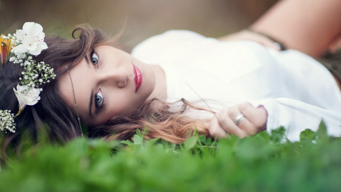 Девушка в белом платье с украшением в волосах лежит на траве