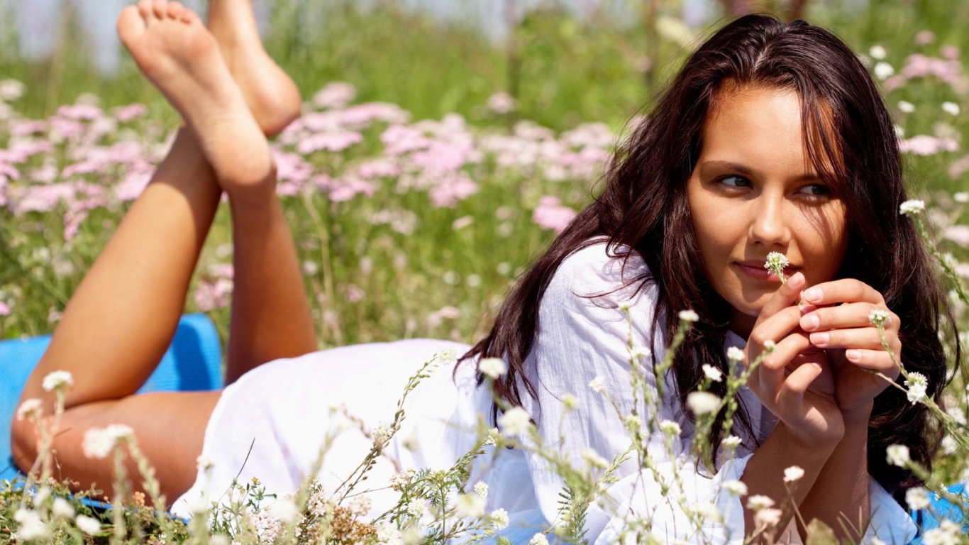 Девушка лежит на животе и держит в руке белый цветок
