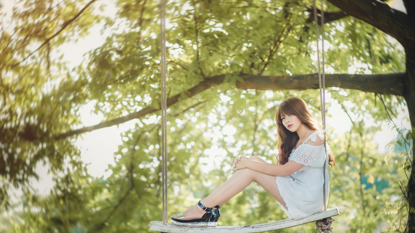 Японская девушка в белом платье сидит на качелях