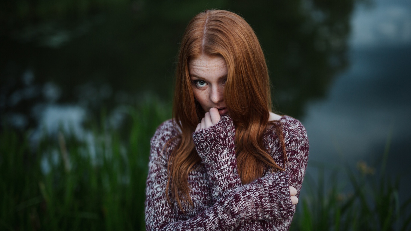Рыжая девушка в свитере на фоне водоема