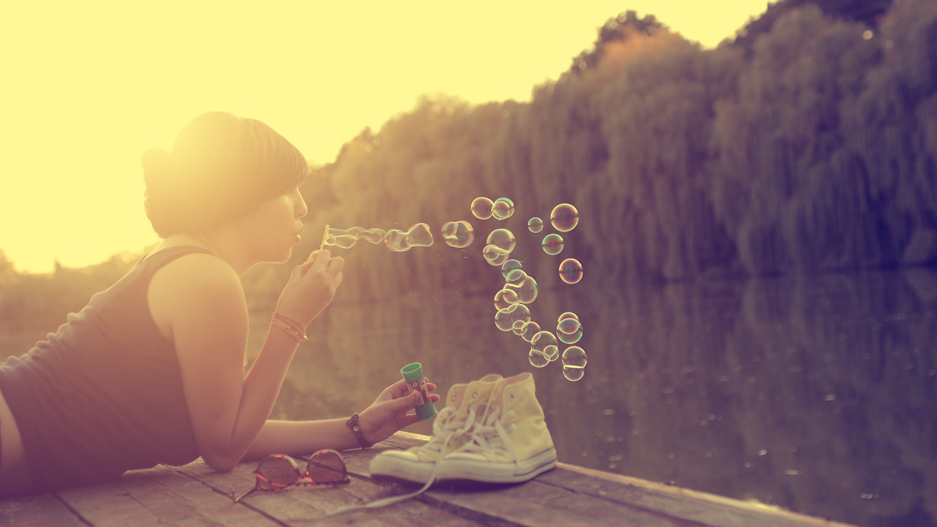 Девушка лежит на пирсе и играет с мыльными пузырями