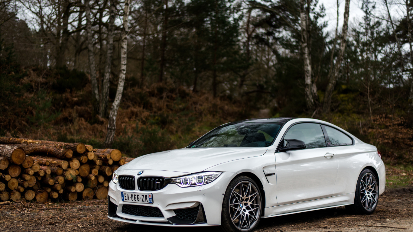 Белый стильный автомобиль BMW M4 на фоне деревьев