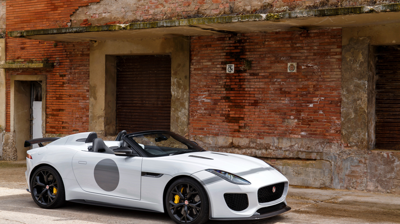 Белый автомобиль Jaguar F-Type у красной кирпичной стены