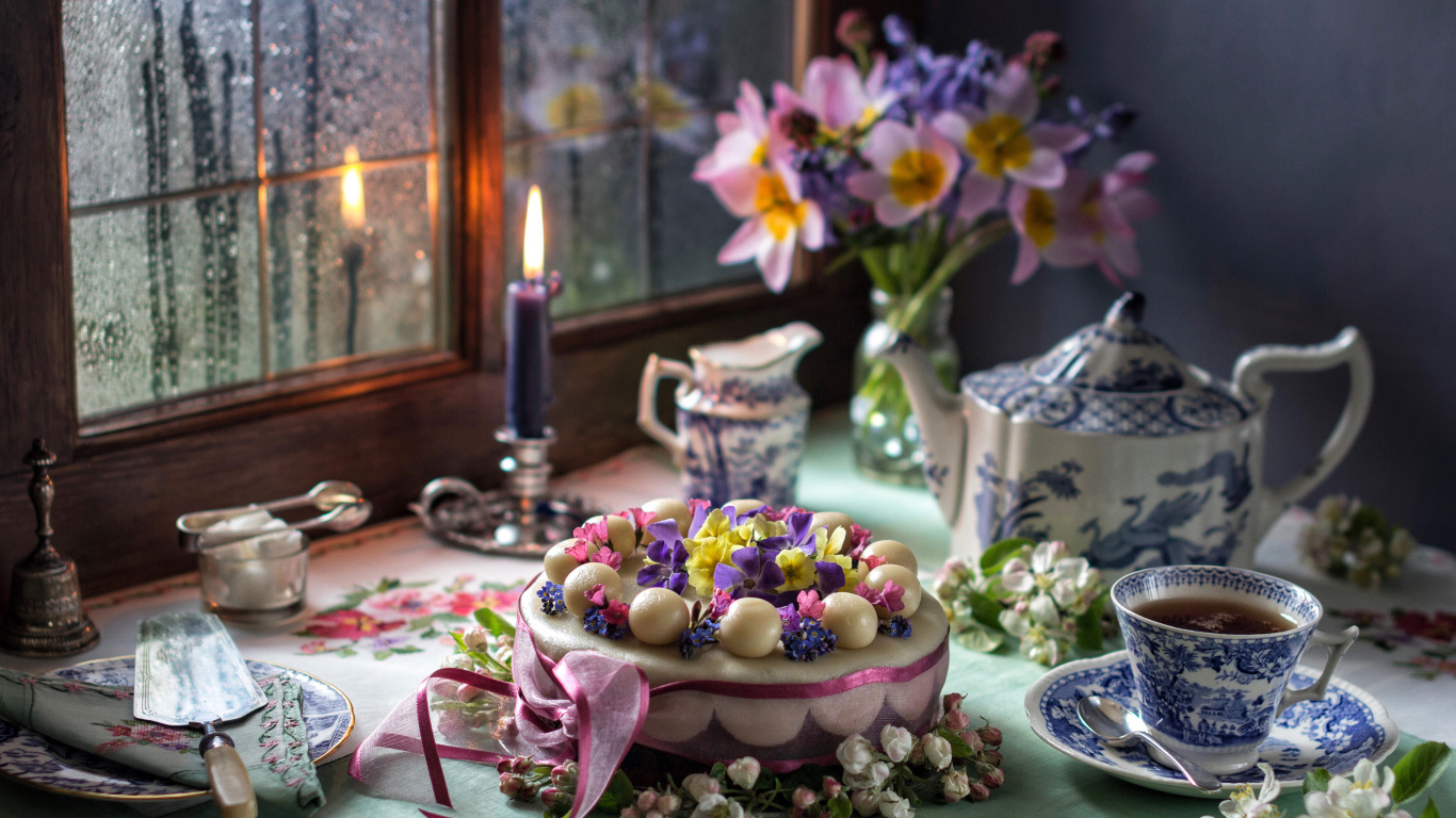 Красивый торт на столе с сервизом и горящей свечой у окна