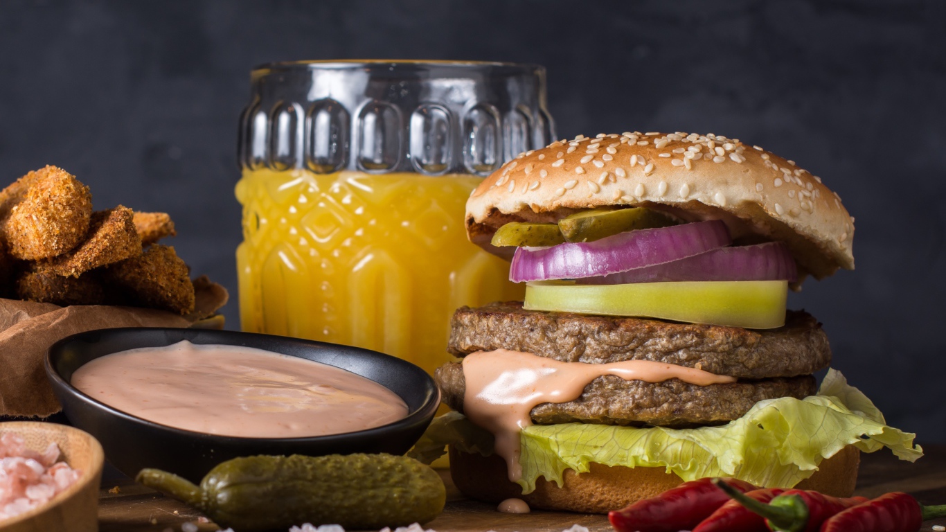 Аппетитный гамбургер на столе с соусом, овощами и соком