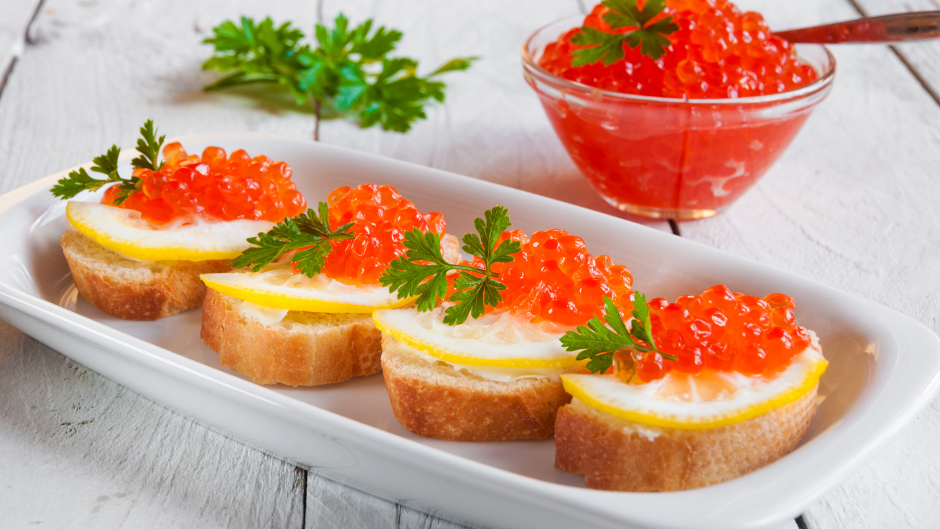 Бутырброды с красной икрой и лимонами на белой тарелке