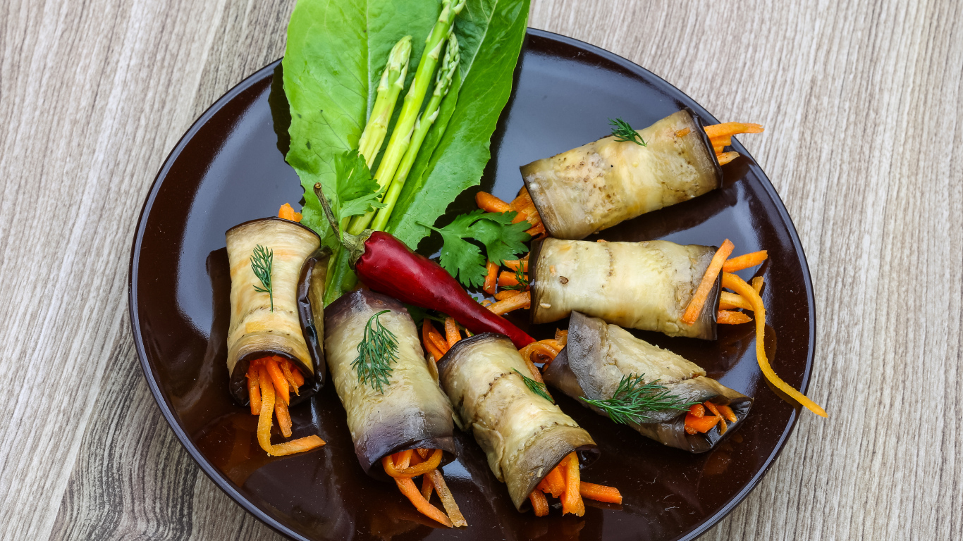 Рулетики из баклажанов с морковью на тарелке с листьями салата