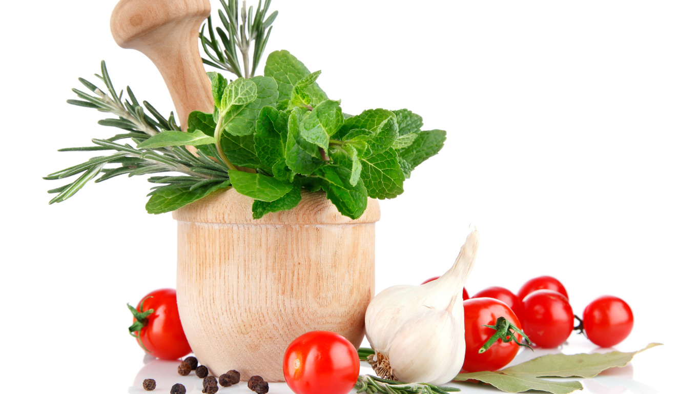 Деревянная ступа и пестик со специями и зеленью на столе с чесноком и помидорами