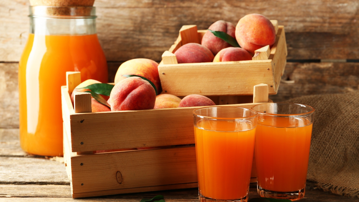 Свежие персики в деревянном ящике со свежим соком на столе