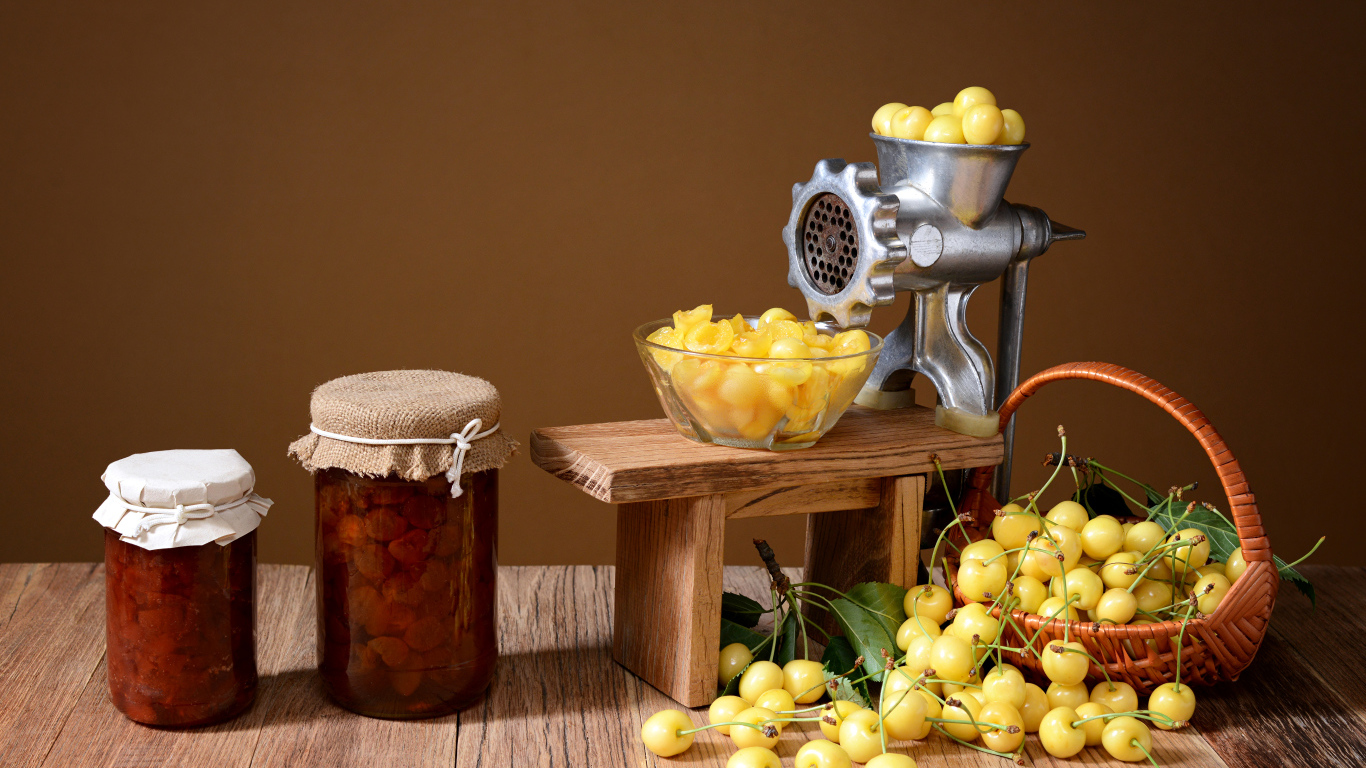 Две баночки варенья и желтые черешни на столе с мясорубкой