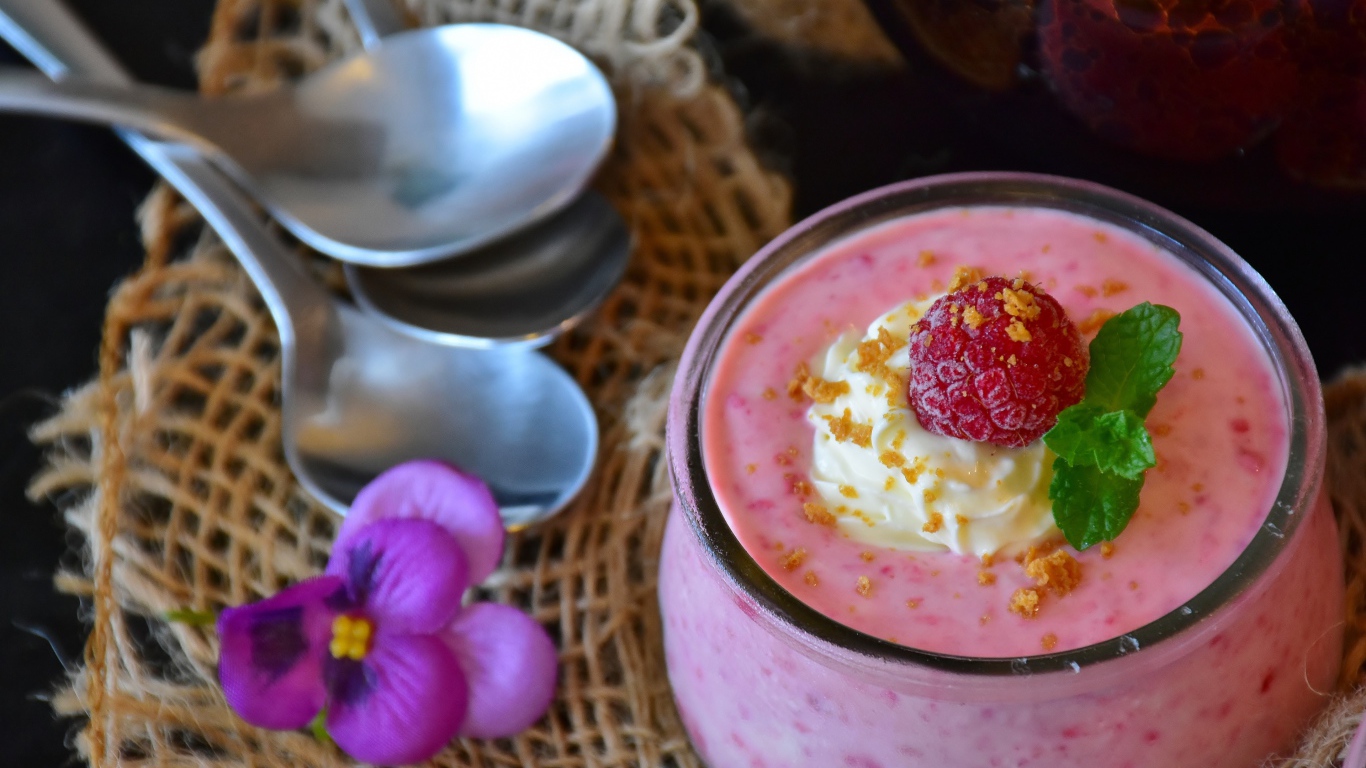 Десерт с малиной и кремом на столе с ложками