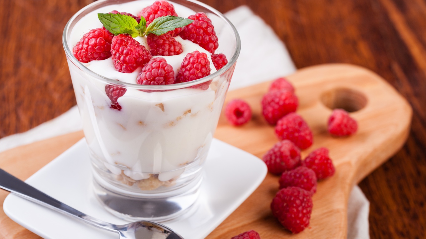 Десерт с йогуртом и свежей малиной в стеклянном стакане на столе