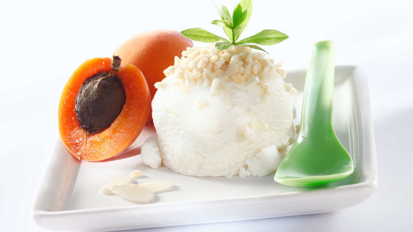 Шарик ванильного мороженого с абрикосами на белой тарелке с ложкой