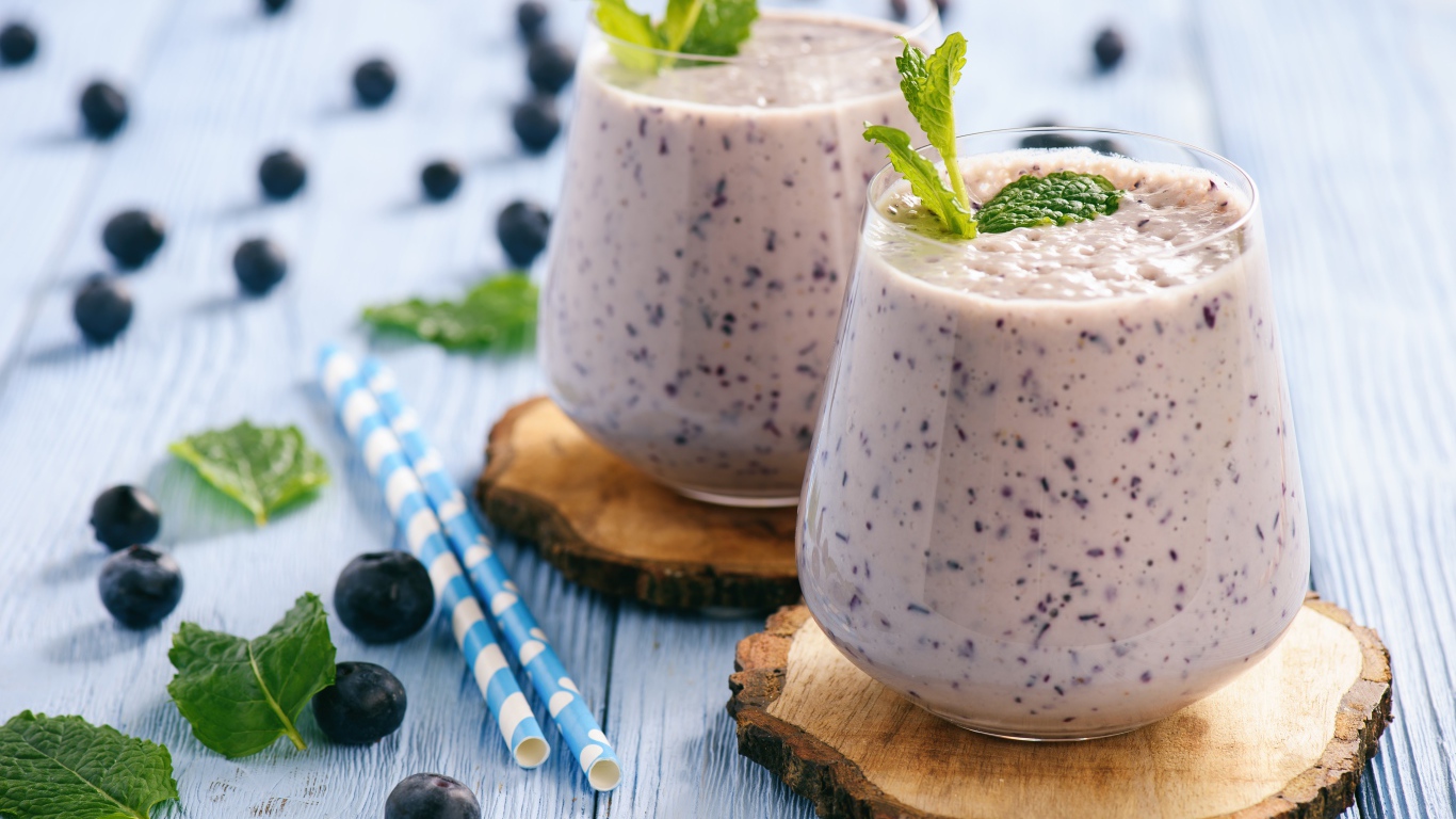 Черничный смузи на столе со свежими ягодами и трубочками