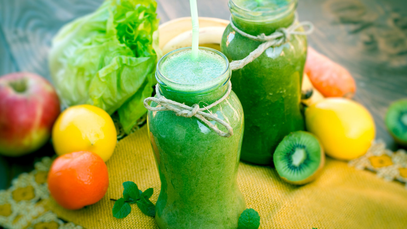 Зеленый смузи в бутылках с трубочками и фруктами на столе