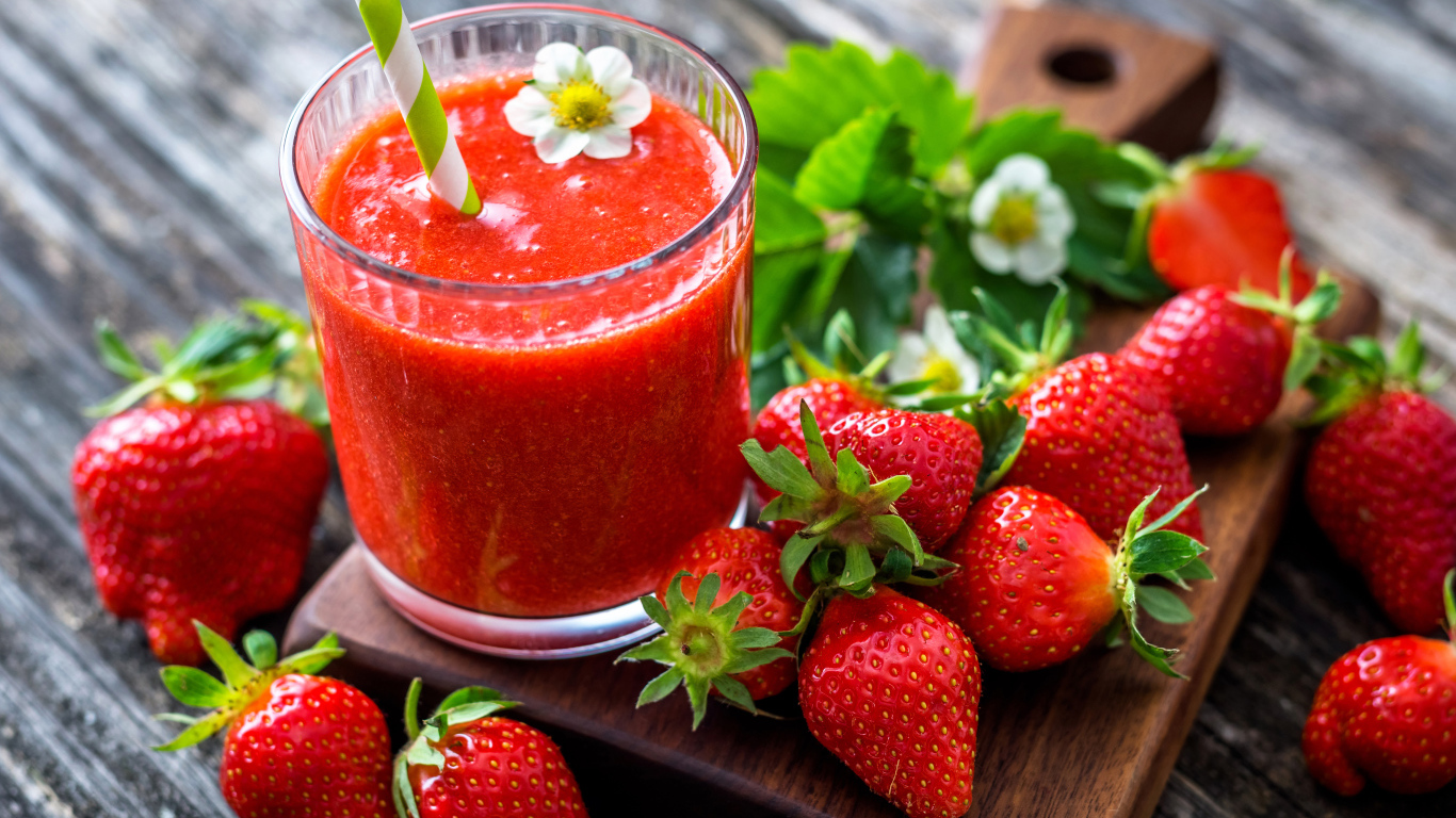 Клубничное смузи с трубочкой и свежими ягодами клубники на разделочной доске