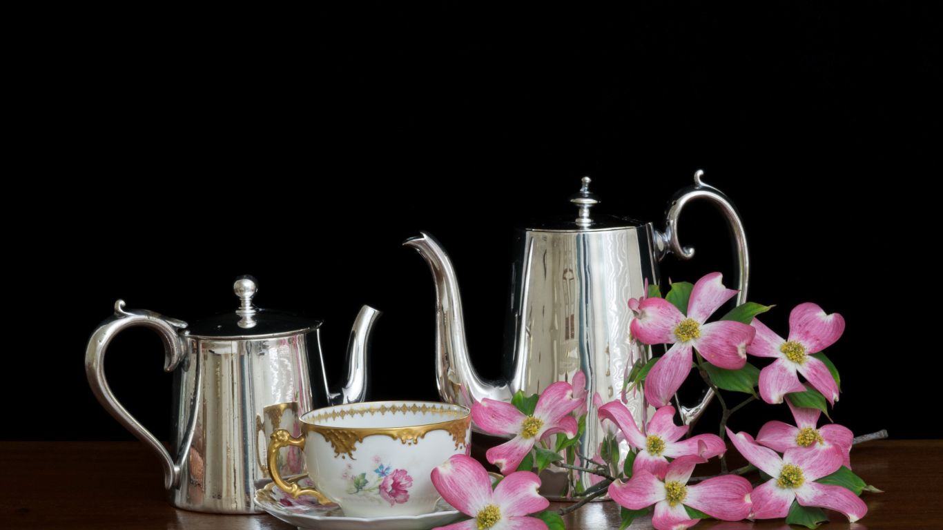 Чайники с чашкой с цветами на столе на черном фоне