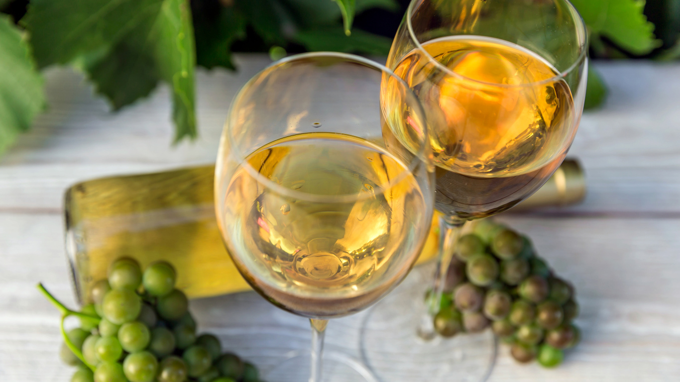Два бокала белого вина с белым виноградом на столе