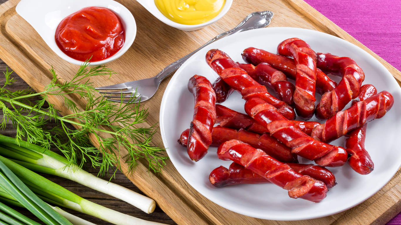 Аппетитные сосиски барбекю на столе с соусом и зеленью