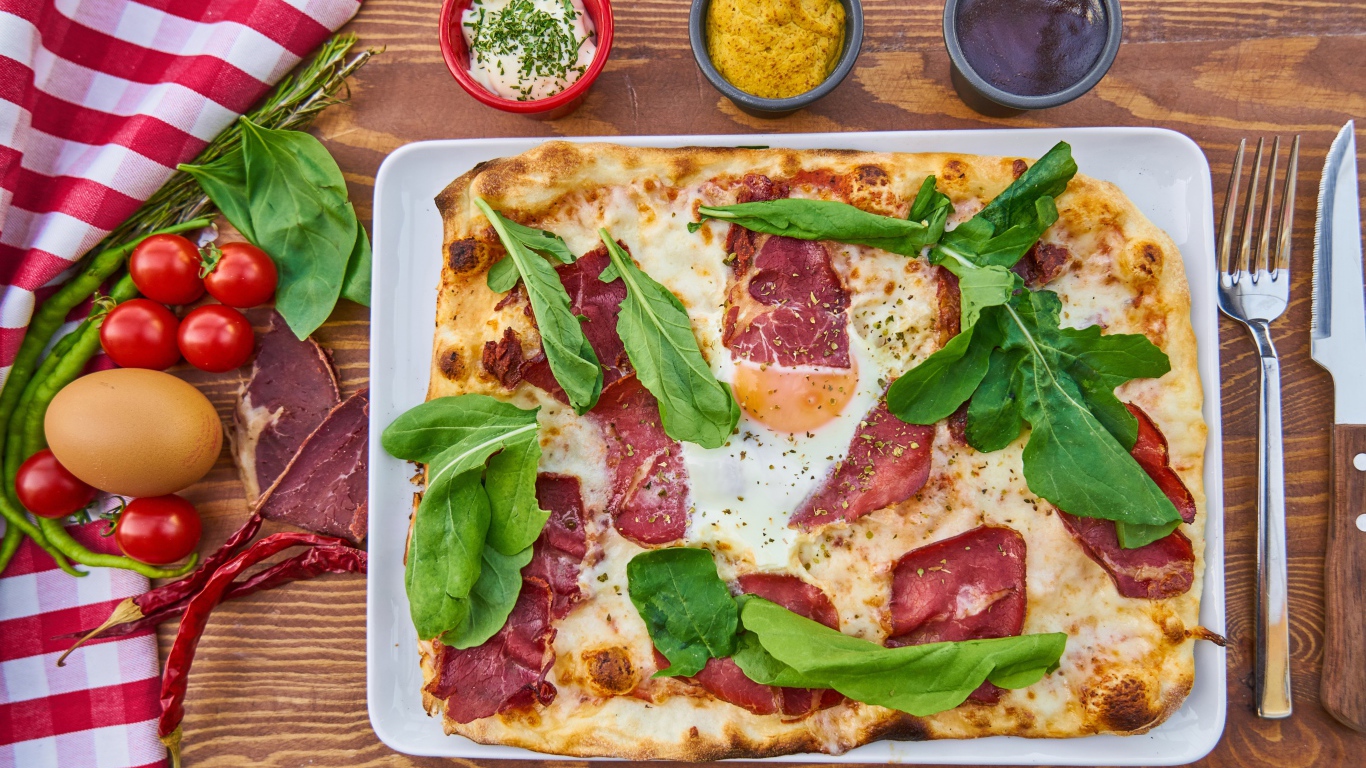 Пицца с беконом и зелеными листьями базилика на столе 