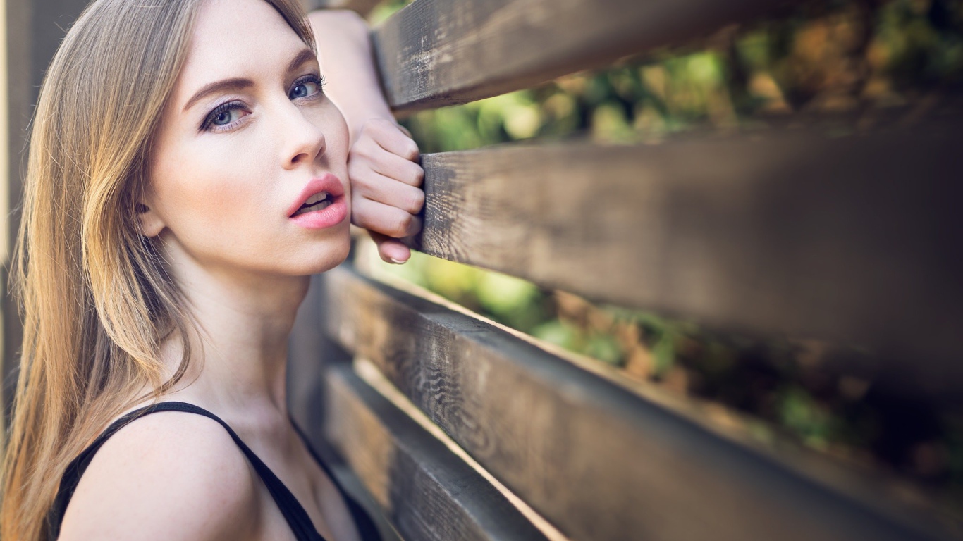 Красивая голубоглазая девушка у деревянного забора 