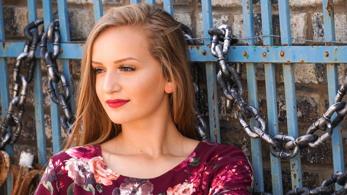 Красивая молодая девушка сидит у забора с железными цепями