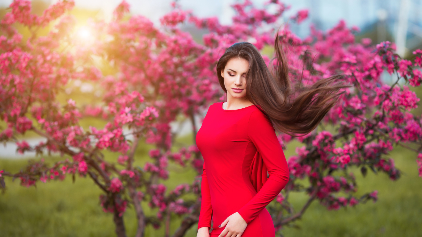 Милая шатенка в красном платье на фоне цветущего дерева