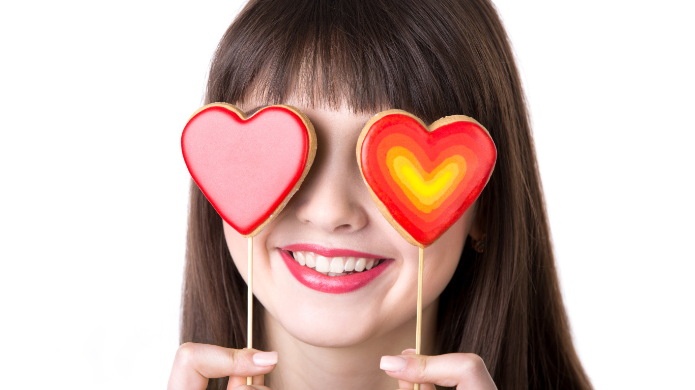 Красивая девушка шатенка закрыла глаза леденцами в форме сердца