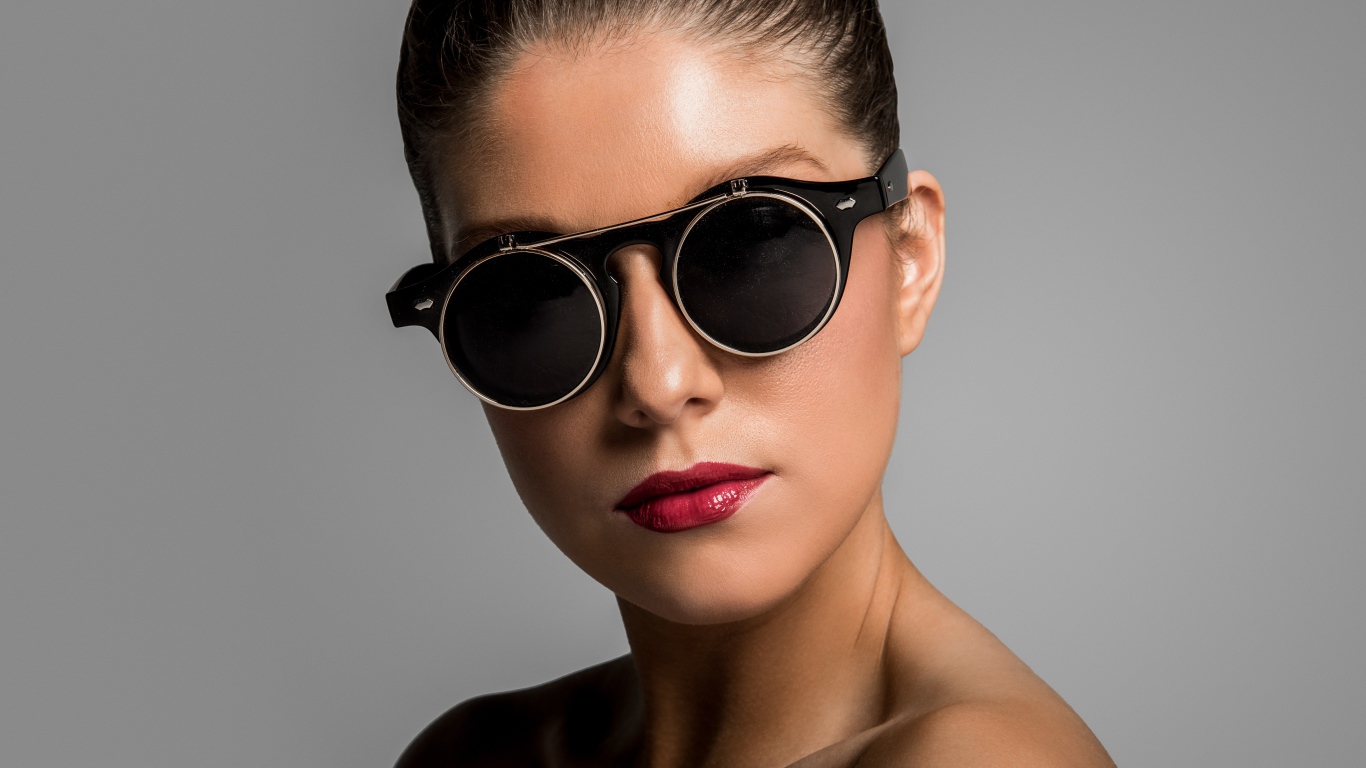Лицо девушки в черных очках на сером фоне