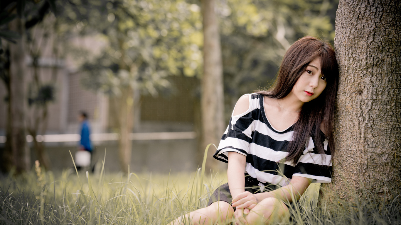 Молодая девушка азиатка сидит на траве у дерева