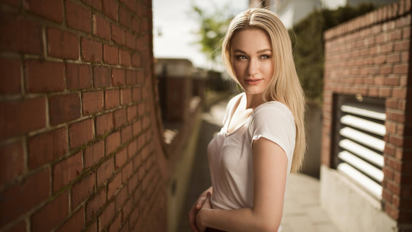 Молодая девушка блондинка у кирпичной стены 
