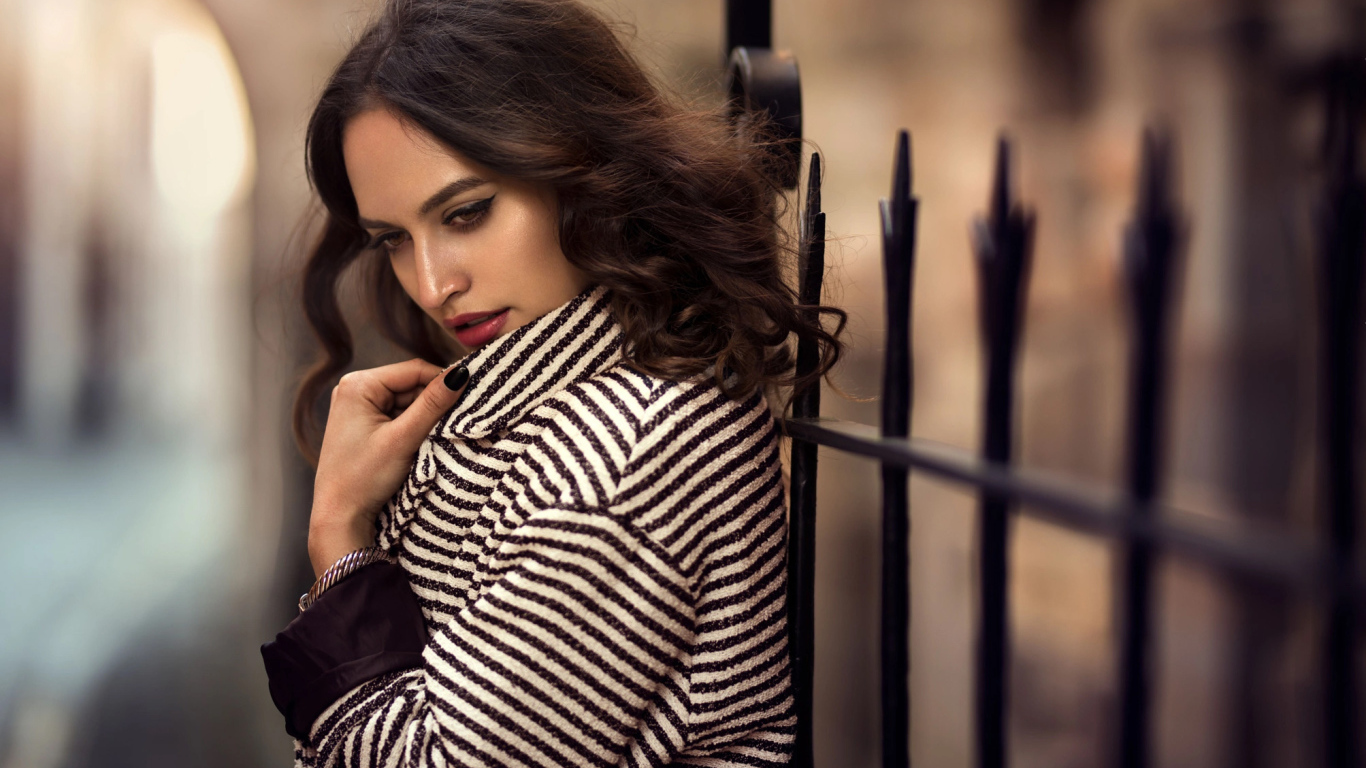 Молодая брюнетка в пальто у забора