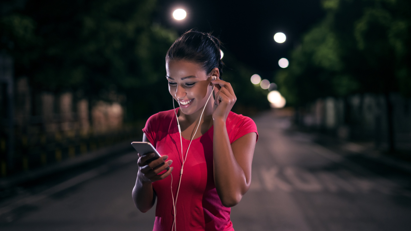 Молодая улыбающаяся девушка в наушниках с телефоном в руках