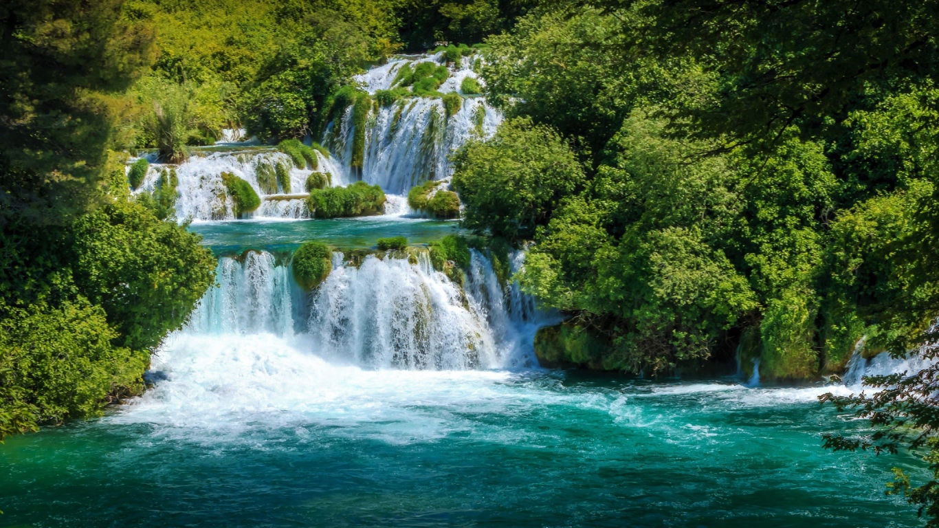 Бушующая голубая вода водопада у зеленых деревьев