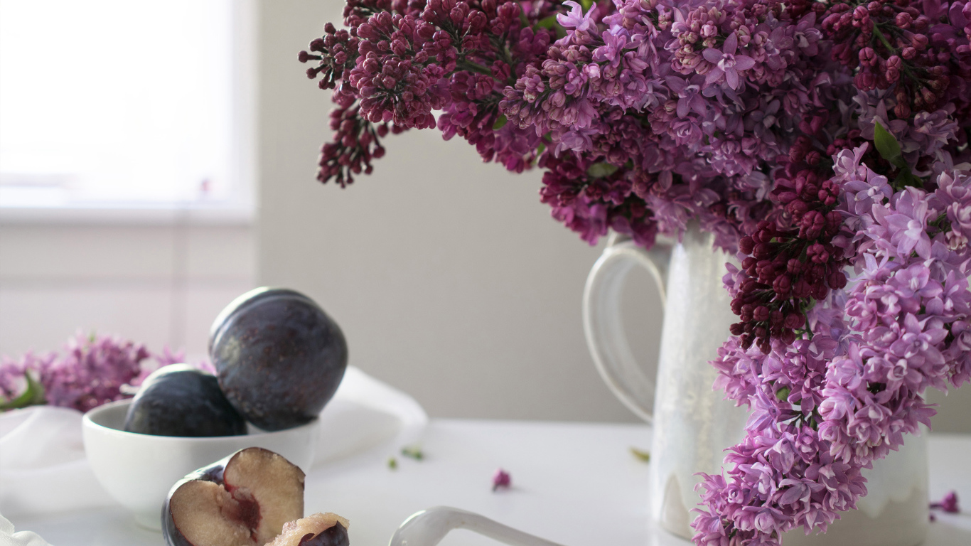 Красивый букет сирени в белой вазе на столе со сливами