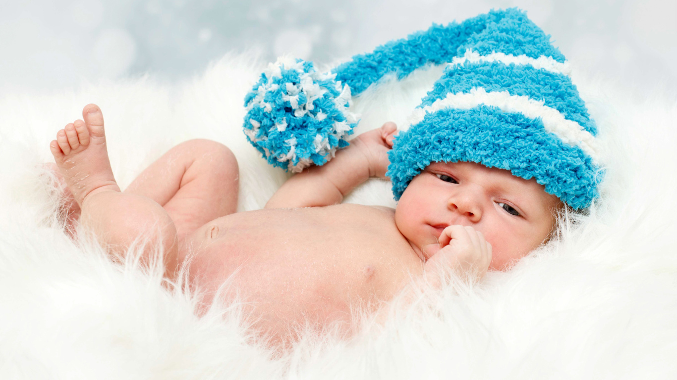 Грудной ребенок в голубой шапке с бубоном на голове