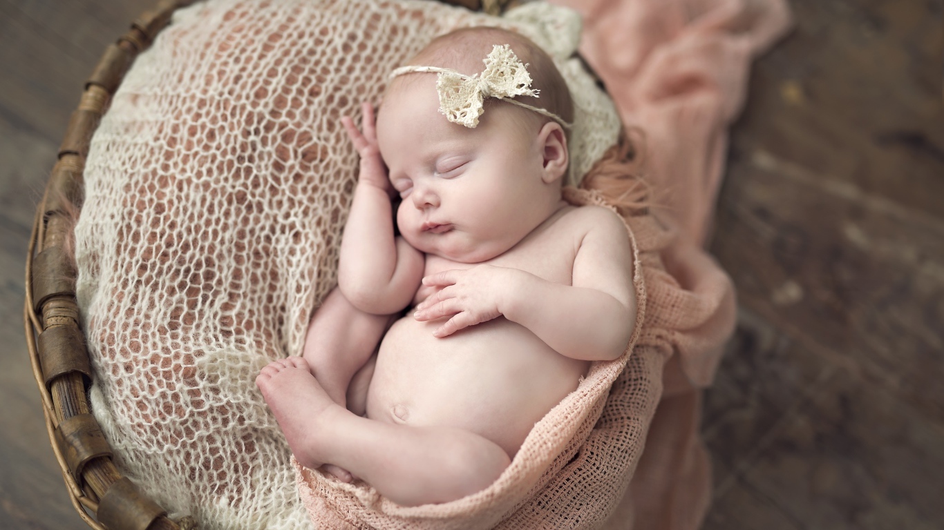 Грудной ребенок с бантиком на голове спит в корзине