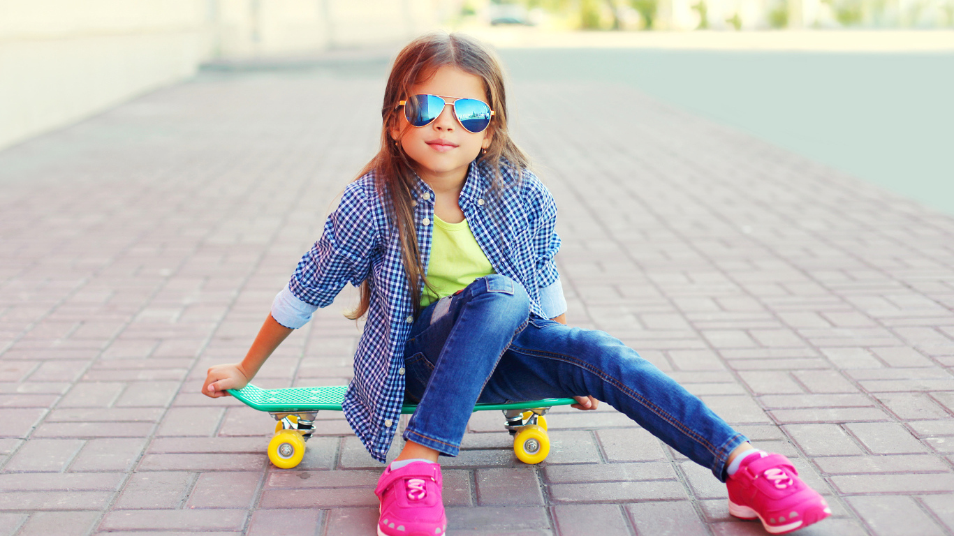 Девочка в солнечных очках сидит на скейтборде