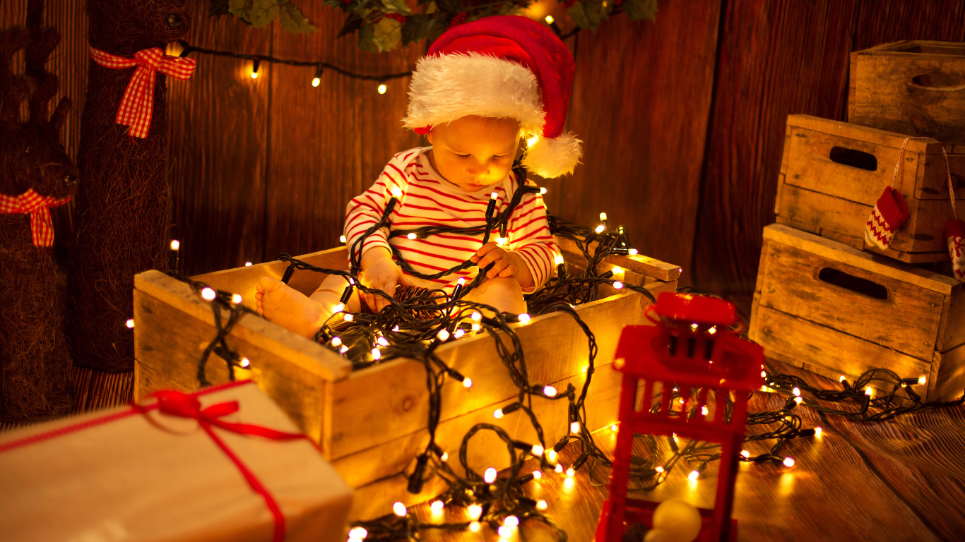 Маленький мальчик сидит в коробке с новогодней гирляндой