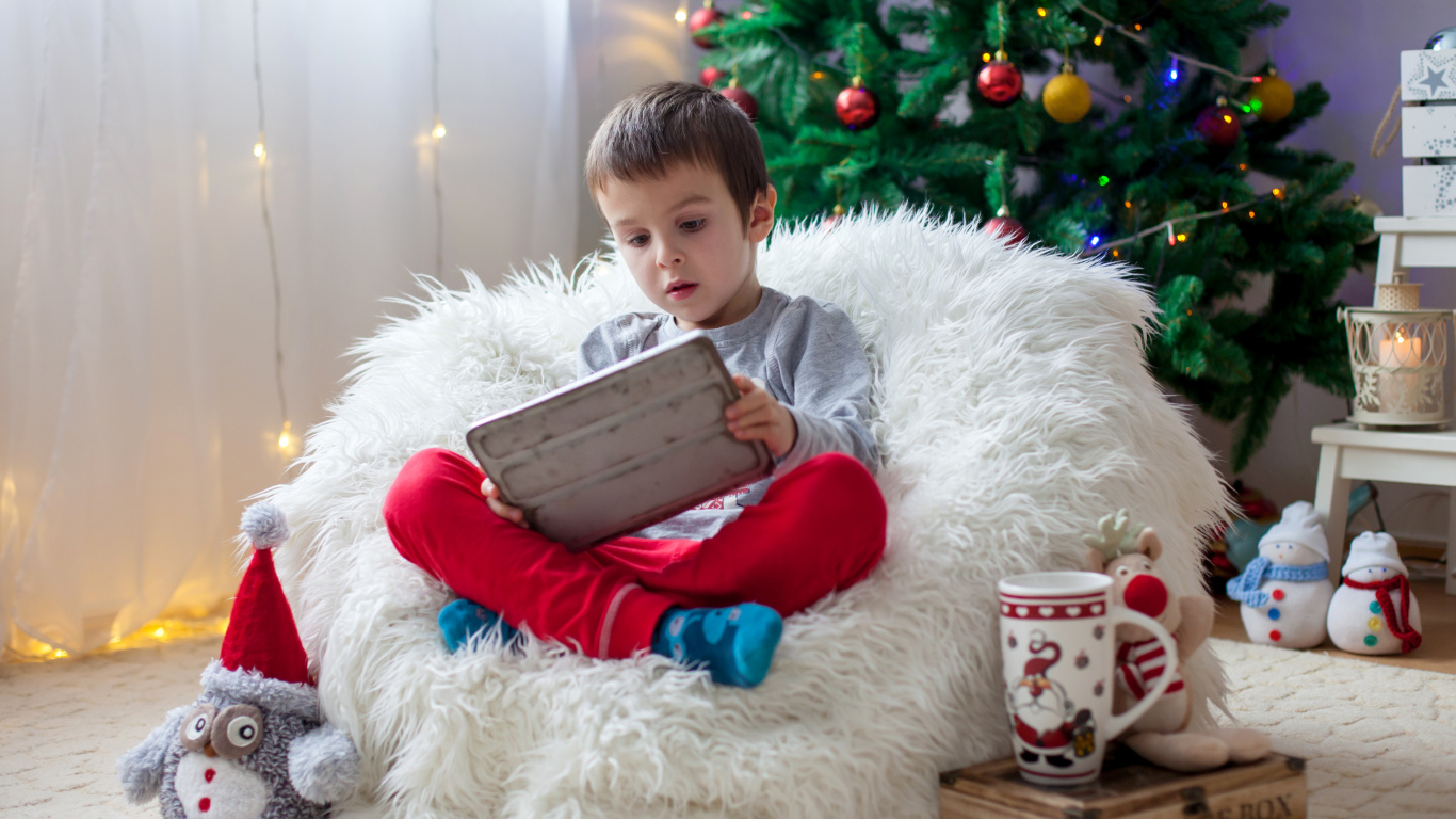 Маленький мальчик сидит в мягком кресле у новогодней елки